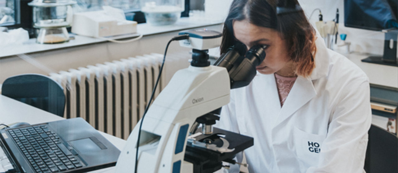 Een student uit de bachelor biomedische laboratoriumtechnologie van HOGENT kijkt door een microscoop.