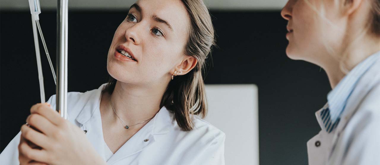 Twee studenten verpleegkunde aan HOGENT aan de slag met een infuus in een ziekenhuisomgeving.