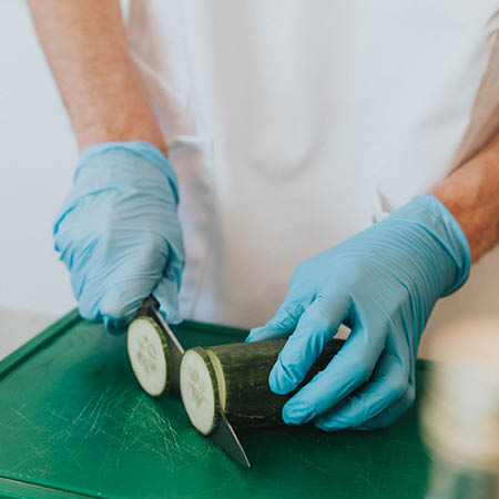 Close-up van de handen van een oud-student voedingstechnologie van HOGENT terwijl hij een courgette snijdt.