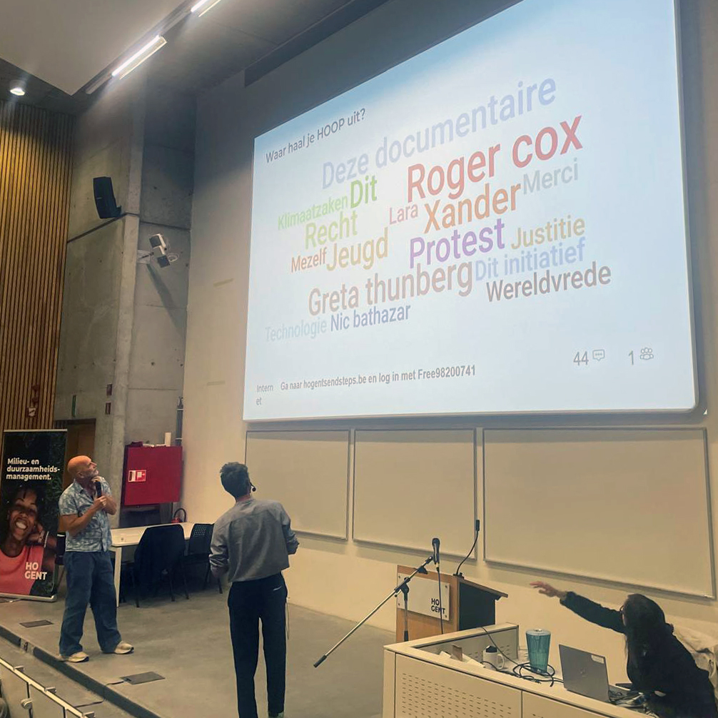 Nic Balthazar en Philippe Thion staan in een auditorium voor een projectiescherm met een woordenwolk van antwoorden van studenten op de vraag "Waar haal je hoop uit?"