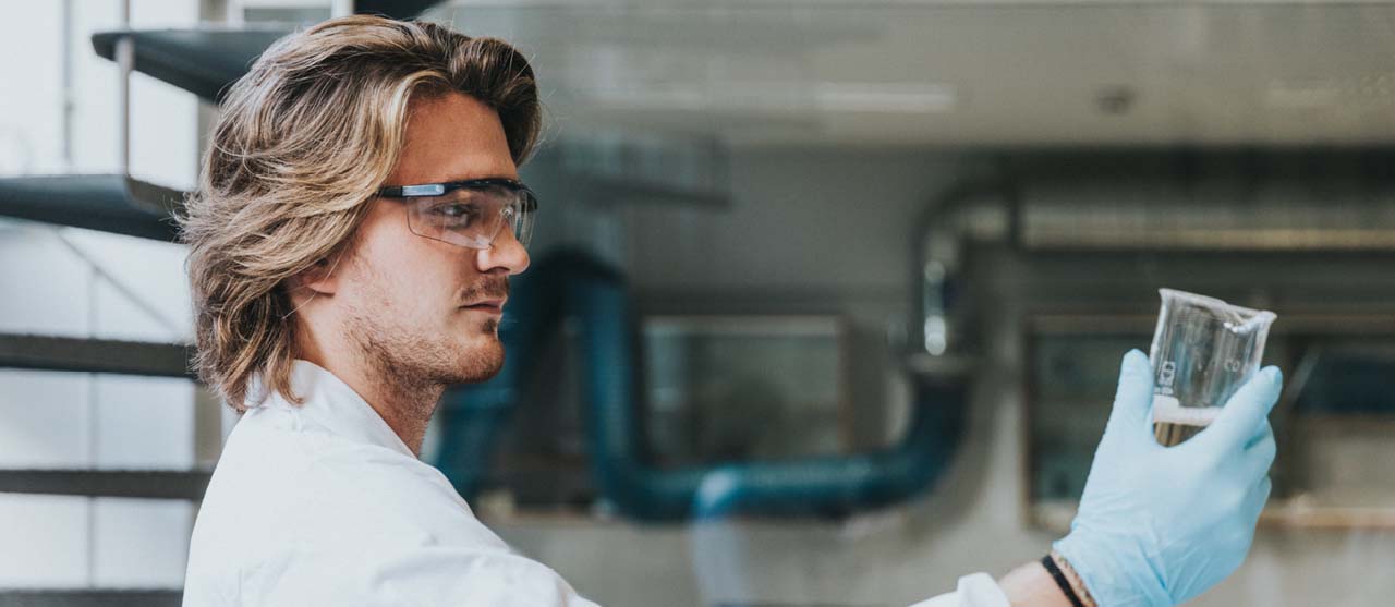 Een student voedingstechnologie controleert een transparante vloeistof in een glazen maatbeker in het voedingslaboratorium van HOGENT.