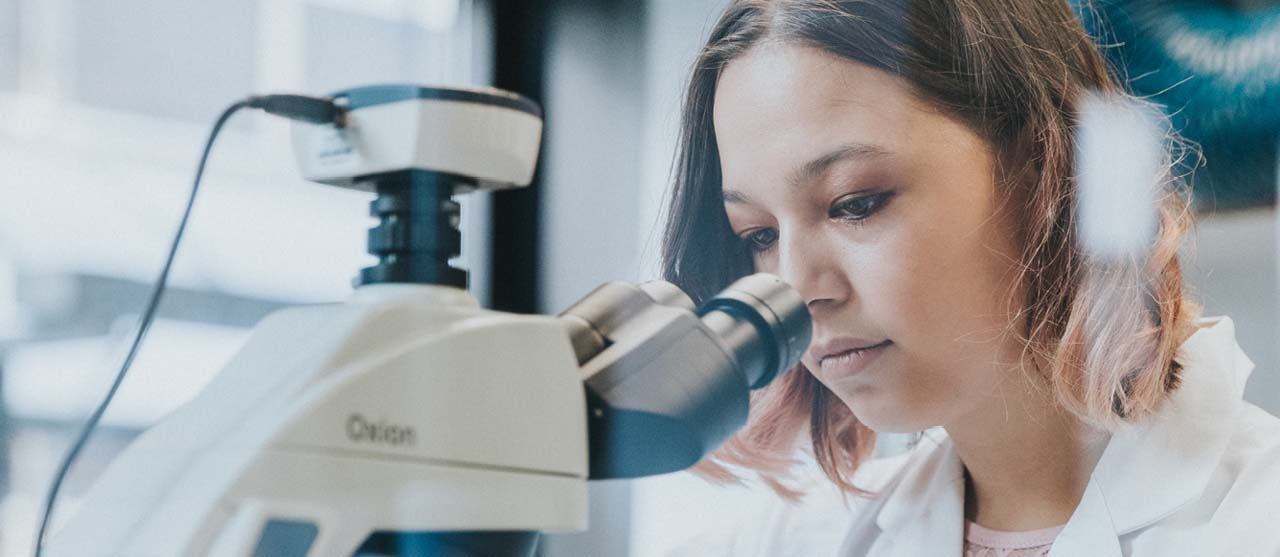 Een studente voedingstechnologie kijkt in een microscoop in het voedingslaboratorium van HOGENT.