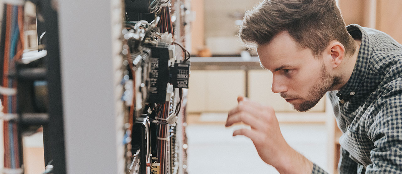 Een student uit de graduaatsopleiding elektromechanische systemen met afstudeerrichting meet- en regeltechnieken aan HOGENT werkt aan een industriële machine om die te automatiseren.