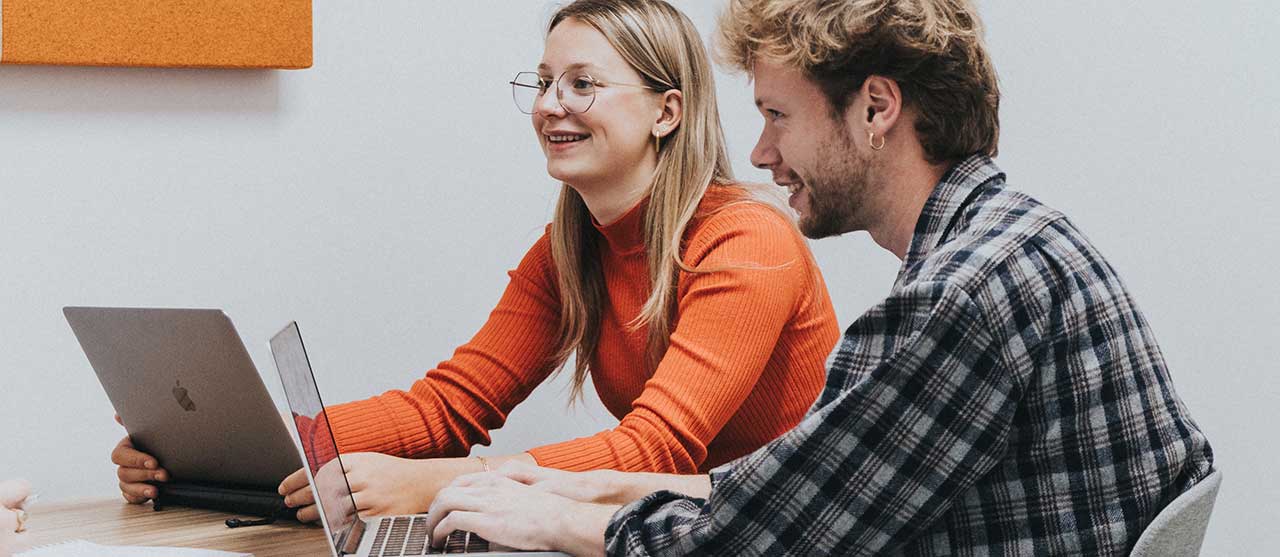 Twee studenten uit het graduaat bouwkundig tekenen aan HOGENT zitten in een overleg en nemen notities op hun laptop.