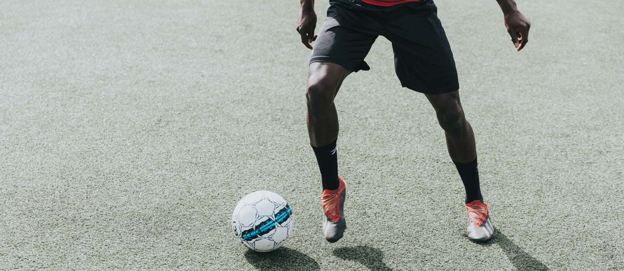 Een student LO en bewegingsrecreatie dribbelt met een bal op het voetbalveld van HOGENT.
