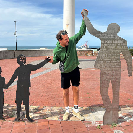 student uit de opleiding orthopedagogie staat op de zeedijk aan een standbeeld, met handen in de lucht