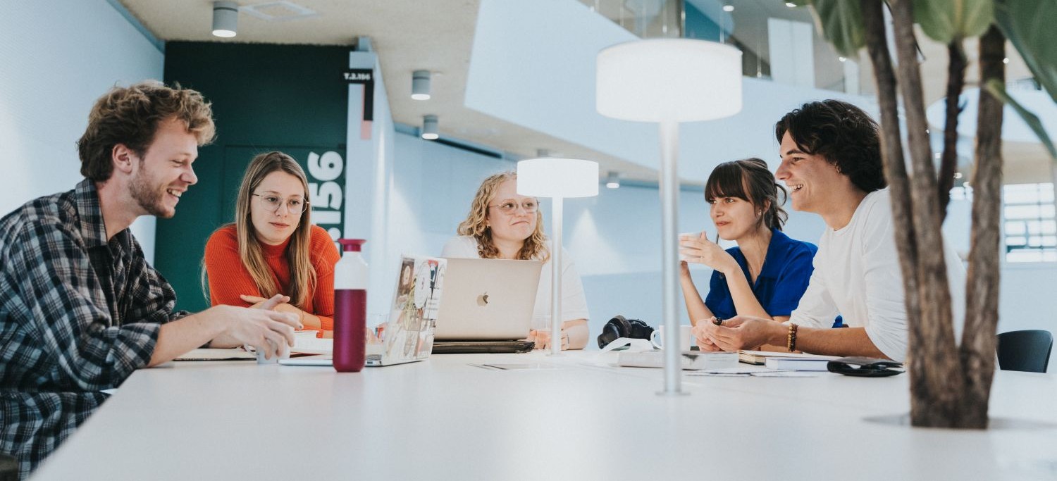 Vijf studenten uit de bachelor sociaal werk die samen aan een tafel samen zitten en werken in het gebouw T van HOGENT