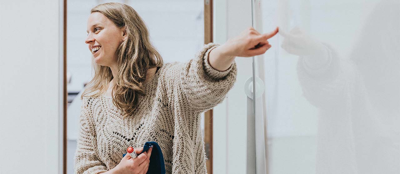 Lesgever textieltechnologie van HOGENT, met breistaal in de hand, wijst naar een tekening op een whiteboard.