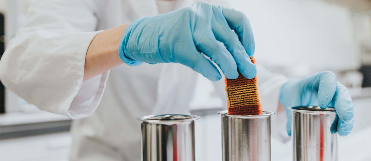 Studente textieltechnologie van HOGENT haalt met handschoenen een stofstaal uit een waskoker in het chemisch labo.